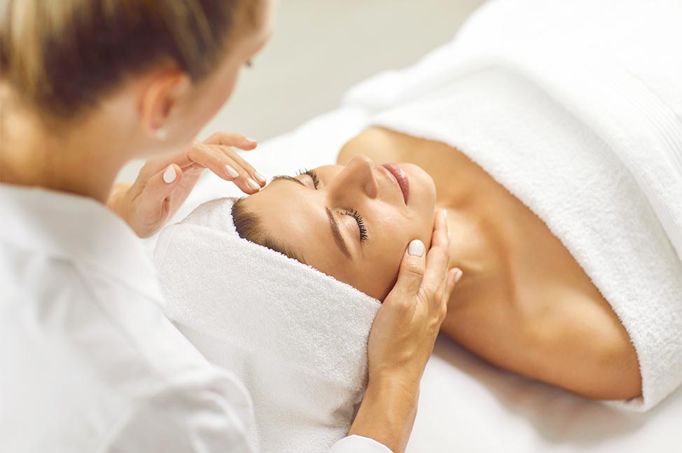 Frau liegt mit geschlossenen Augen und erhält eine Gesichtsbehandlung in einem Spa.
