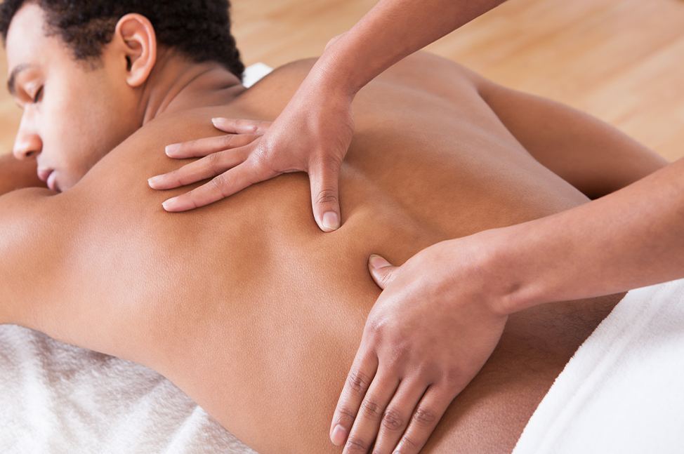 Un homme détendu est allongé sur une table de massage, recouvert d'une serviette blanche. Les mains du thérapeute effectuent des mouvements fermes et précis sur son dos, ciblant les muscles pour offrir une relaxation profonde et revigorante, dans un cadre